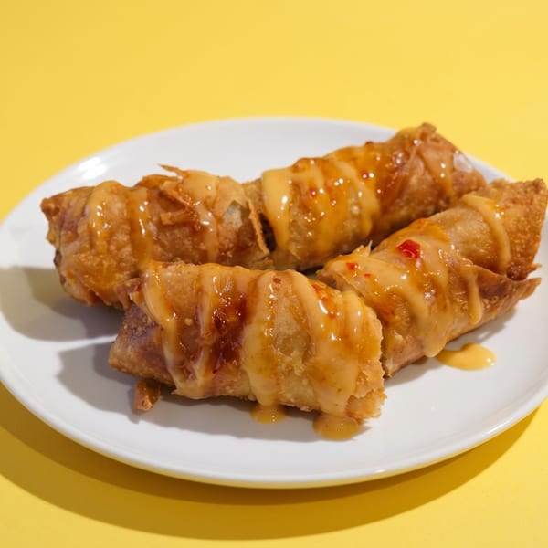 Four crispy fried spring rolls drizzled with a creamy orange sauce on a white plate.